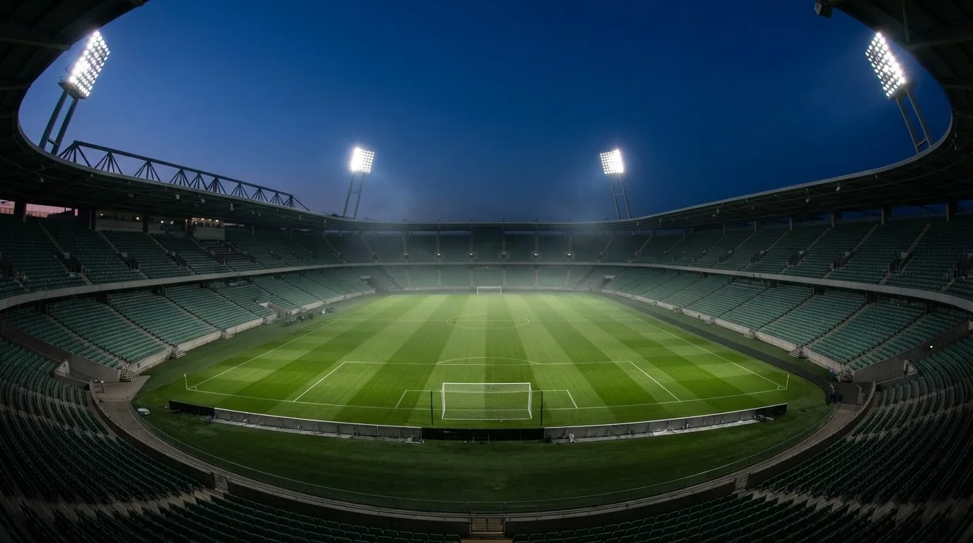 An empty football stadium with floodlight masts at dusk